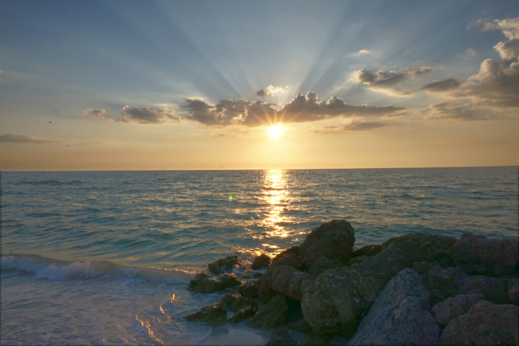 This photo shows a sunset over the ocean with rays light bursting from behind a cloud.