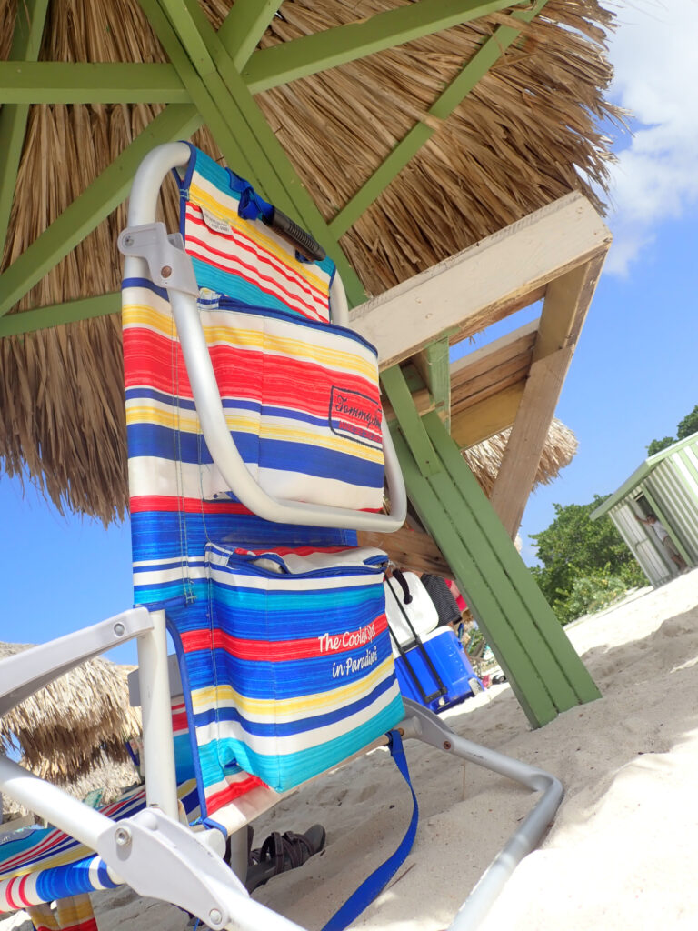 This photo shows a beach chair sitting in the sand, under a palapa.