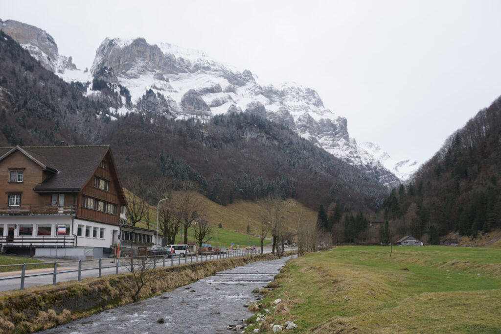 A building set in a mountain valley with a stream running through, located below the Ebenalp mountain peak in Switzerland.