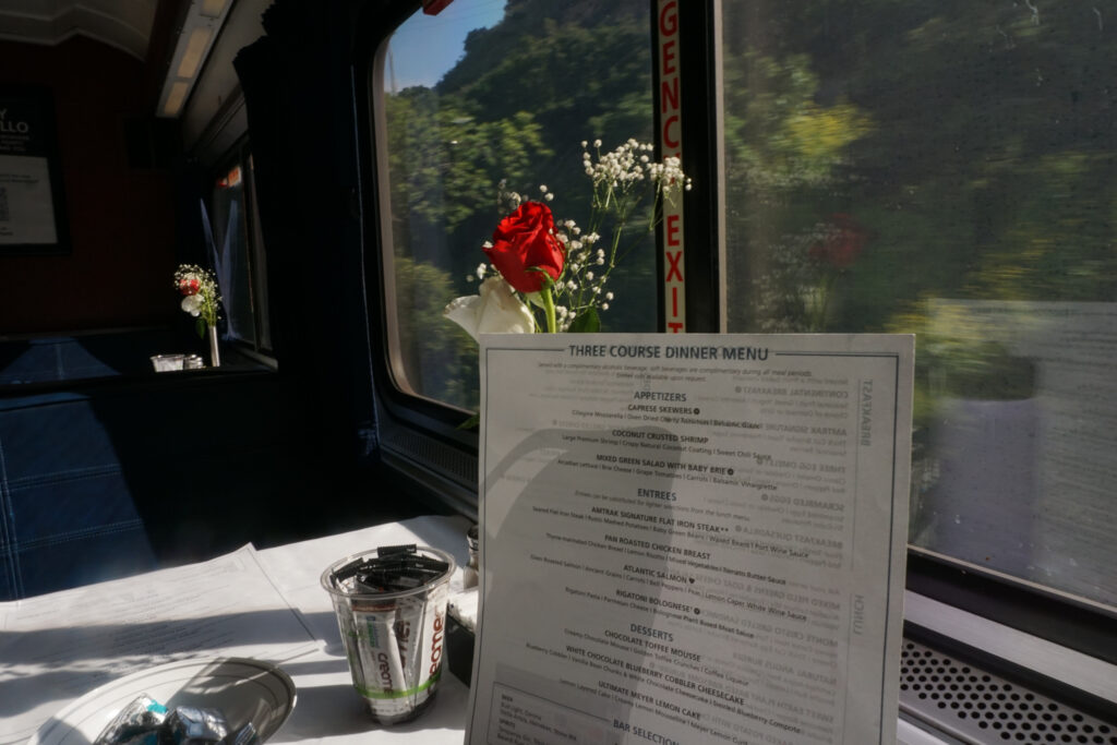 Three-course dinner menu propped against a vase of flowers in the foreground of the train window.