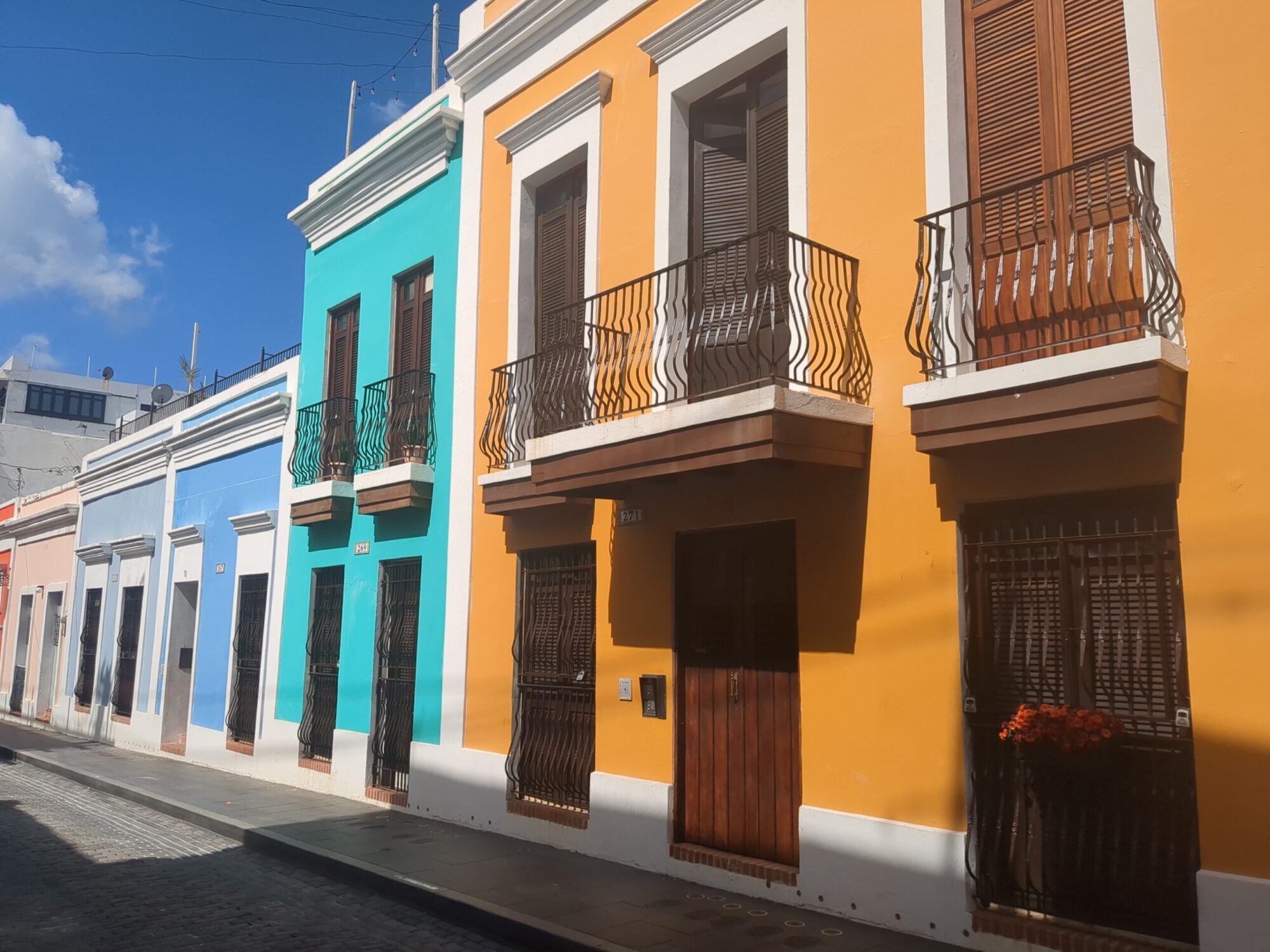 Buildings in Old San Juan with metal balconies and wood shutters and painted different colors: orange, aqua, light blue, lighter blue, and pink.