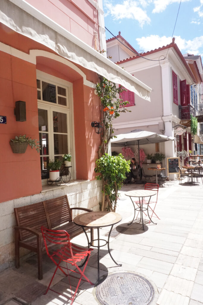 A cafe in Nafplio with a pink exterior and bougainvillea hanging against the wall